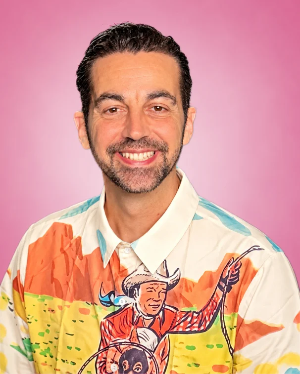 Scot Nery smiling in a colorful western print shirt against a pink background