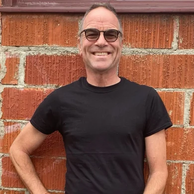 Gig Entertainer Ramp smiling in a black t-shirt and glasses in front of a brick wall