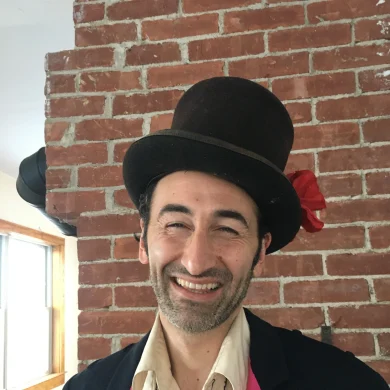 Gig entertainer Ramp smiling in front of a brick wall wearing a top hat with a red flower